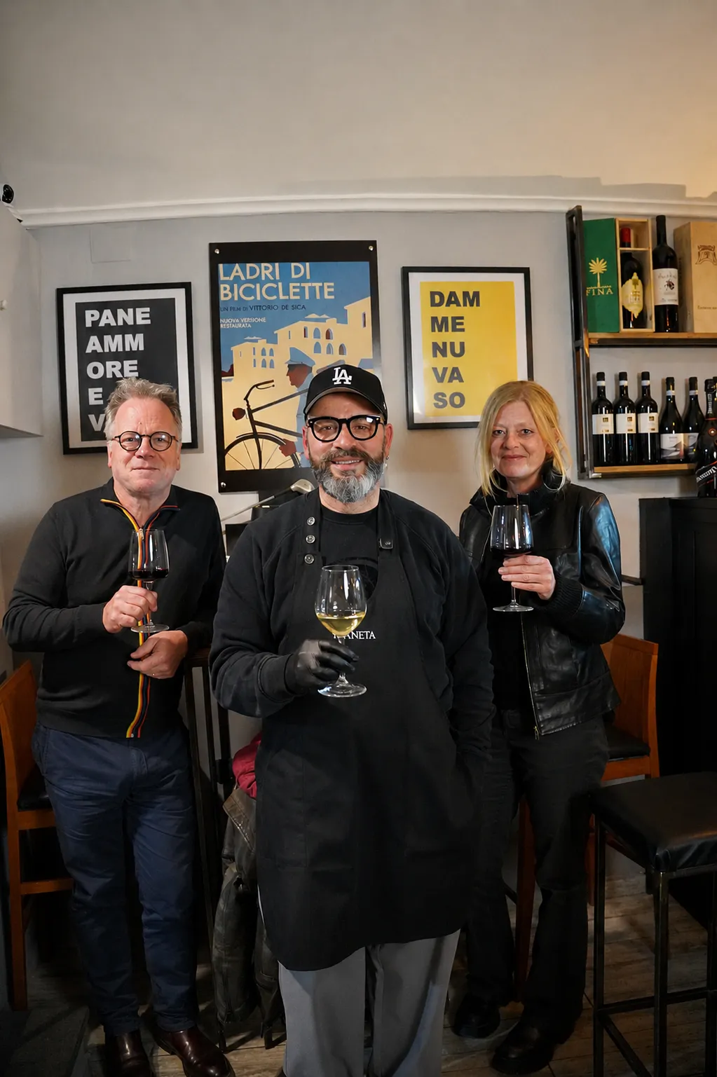 Marcello insieme a due clienti con i calici in mano nel suo wine bar
