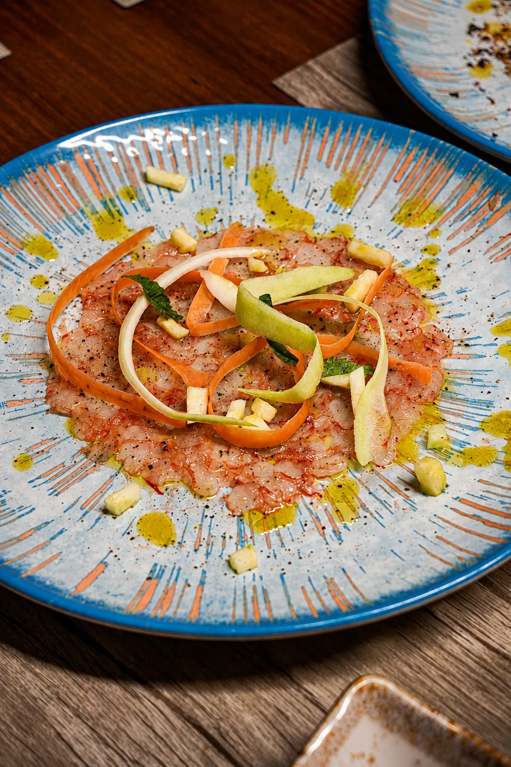 Tartare di gambero con carote e mela verde su piatto in ceramica dipinta